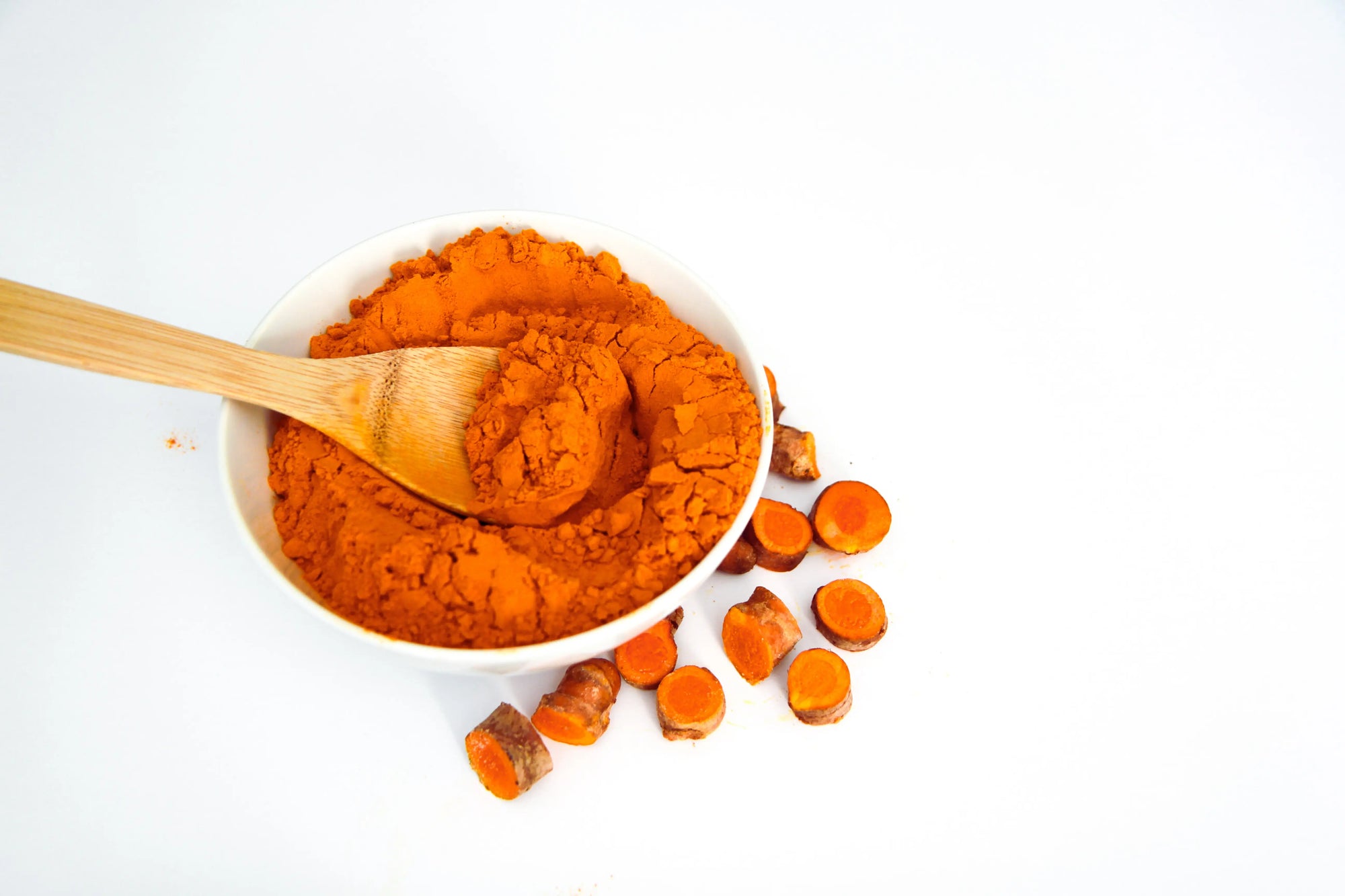 Kurkuma Pulver im Mörser mit Holzlöffel, daneben frische Gelbwurz geschnitten